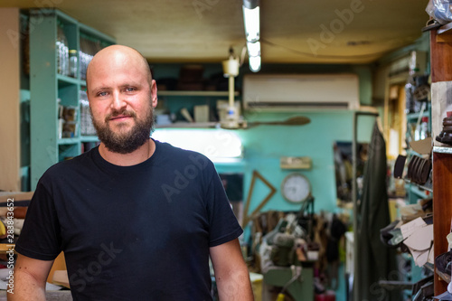 Portrait of a bald mand with beard, shoemaker looking camera at his workshop.