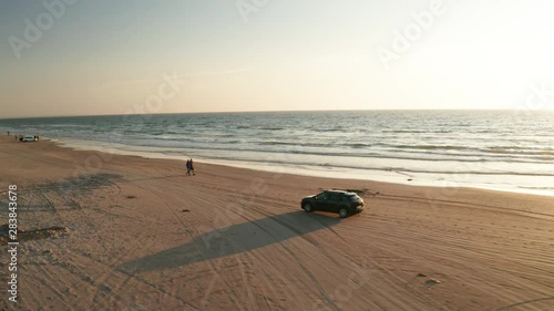 Car driving on the beach next to the ocean sun down