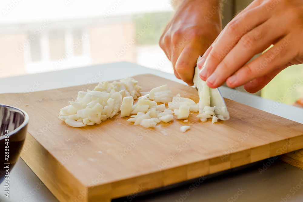 Hands chopping onion in wooden board