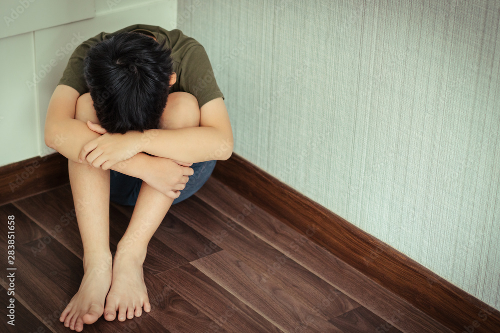 Young Asian preteen/teenage boy sitting at the corner of a room feeling lost. He has his face down and crying. Cyber Bullying, Teen problems, Loneliness, Traumatic, Stressed, frustrated and lost. Young Asian preteen/teenage boy sitting at the corner of a room feeling lost. He has his face down and crying. Cyber Bullying, Teen problems, Loneliness, Traumatic, Stressed, frustrated and lost.