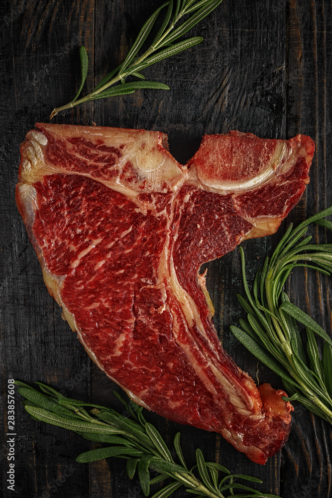 Raw fresh beef T-bone steak and seasoning on dark background. Top view.