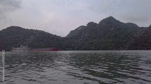 Panoramic view over the sea level in Halong Bay. Cruise and container boat  floating, sailing in emerald water. Limestone cliff covered by green lush jungle rainforest. Vietnam famous destination. photo