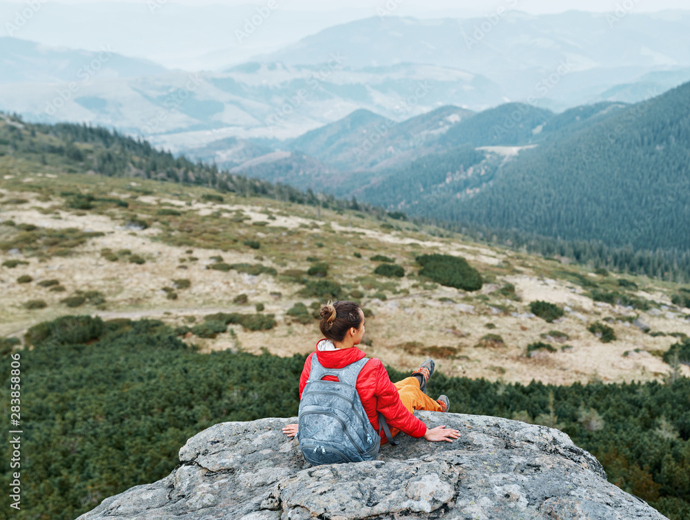 woman hiker in red jacket sitting on the cliff in mountains and meditating