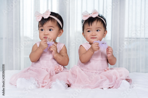 two twin babies in pink dress on bed photo