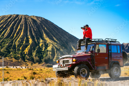 Traveller sit and take a photo on a vintage off road car with Bromo mountain background photo