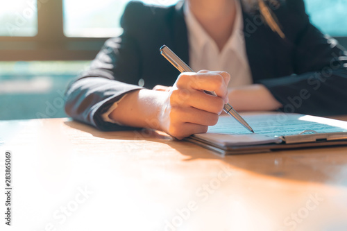 Hand of businesswoman sitting at the table and writing on business contract in office.