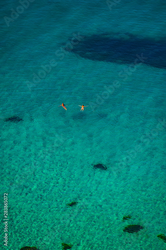 couple of people swimming in the sea on a sunny day in shallow water.