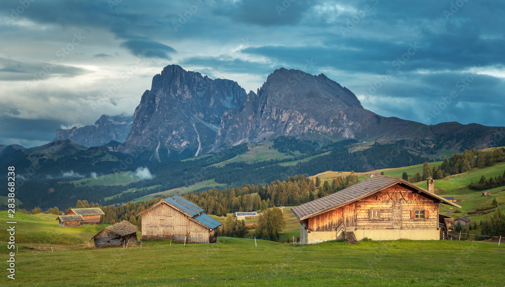 Alpe di Siusi - Seiser Alm with Sassolungo - Langkofel mountain group in background at sunset. Wooden chalets in Dolomites, Trentino Alto Adige, South Tyrol, Italy, Europe