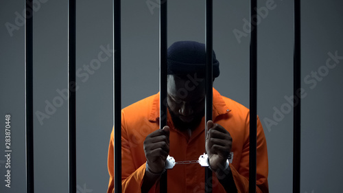 Fotografija Upset afro-american criminal in handcuffs holding prison bars, regretting past