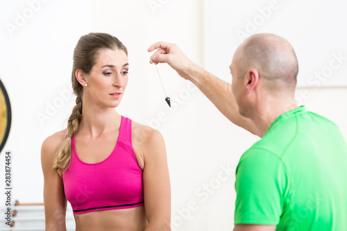Healthy woman looking at man holding pendulum tool