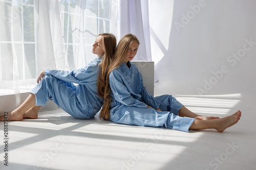two young twin girls in identical blue suits sitting on white cyclorama floor in studio in pattern of light and shadow © Artem Zatsepilin