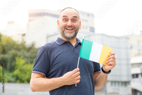 Portrait of a mature man with a beard with the flag of Ireland on a city street. Irish patriot. Football fan.