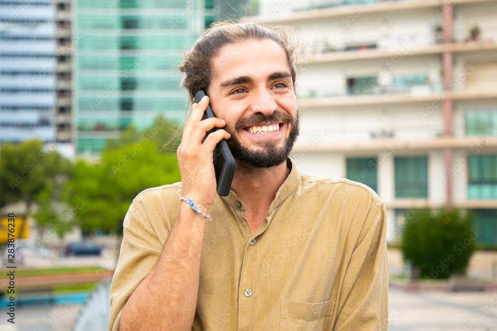 Joyful carefree hipster guy enjoying phone conversation outside. Young man in casual talking on cellphone in city. Phone talk or good news concept Joyful carefree hipster guy enjoying phone conversation outside. Young man in casual talking on cellphone in city. Phone talk or good news concept
