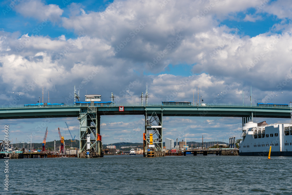 Summer seascape view of Gota Alvbron in Gothenburg Sweden. Traffic bridge with buses and ships against cloudy blue sky.