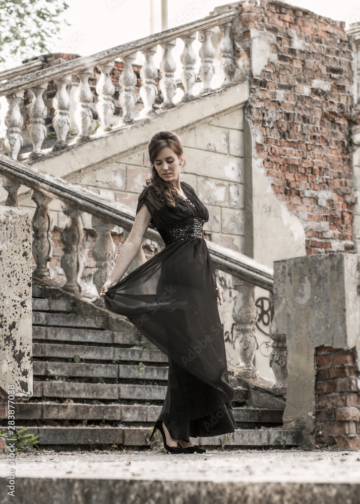 Beautiful girl in a black evening dress on the steps of an abandoned palace. Pretty woman with scars. Young girl in retro style. Pretty Woman