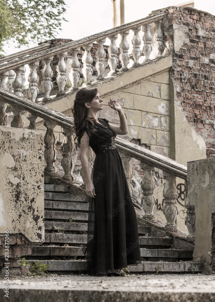 Beautiful girl in a black evening dress on the steps of an abandoned palace. Pretty woman with scars. Young girl in retro style. Pretty Woman