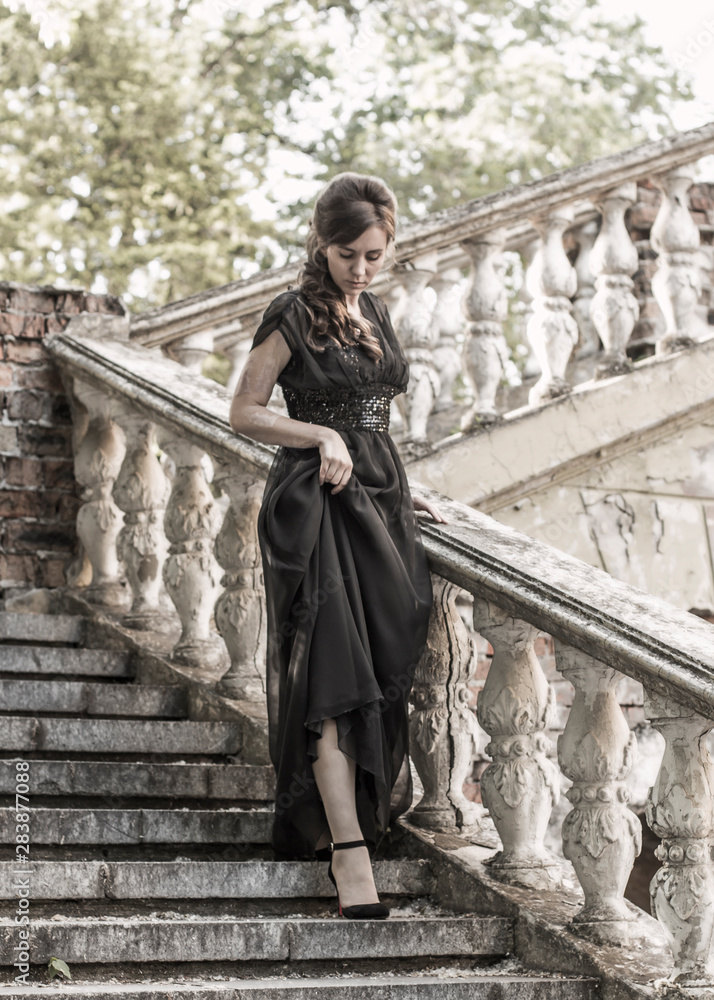 Beautiful girl in a black evening dress on the steps of an abandoned palace. Pretty woman with scars. Young girl in retro style. girl steps up the stairs. Pretty Woman