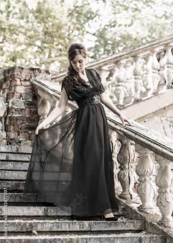 Beautiful girl in a black evening dress on the steps of an abandoned palace. Pretty woman with scars. Young girl in retro style. girl steps up the stairs. Pretty Woman © ppvector