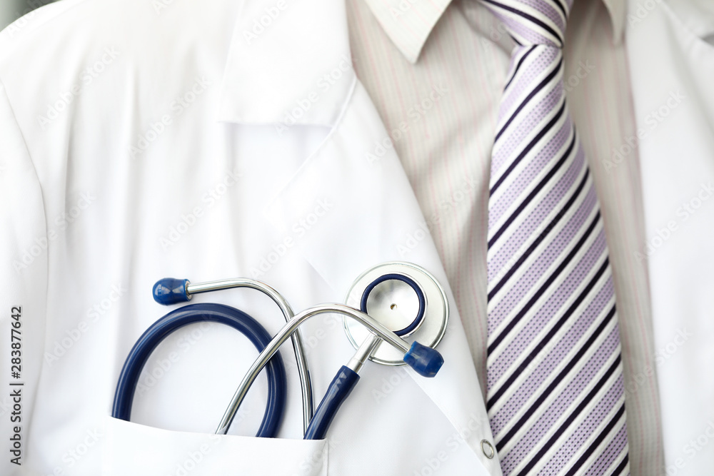 Male GP wearing tie holding stethoscope in smock pocket Male GP wearing tie holding stethoscope in smock pocket