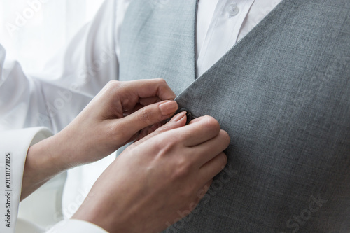 Bride hand holding  buttoning white wedding shirt.Couple getting ready for wedding ceremony.