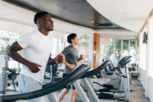 Photo Side view of multiracial sportsmen working out on treadmills in gym on daytime
