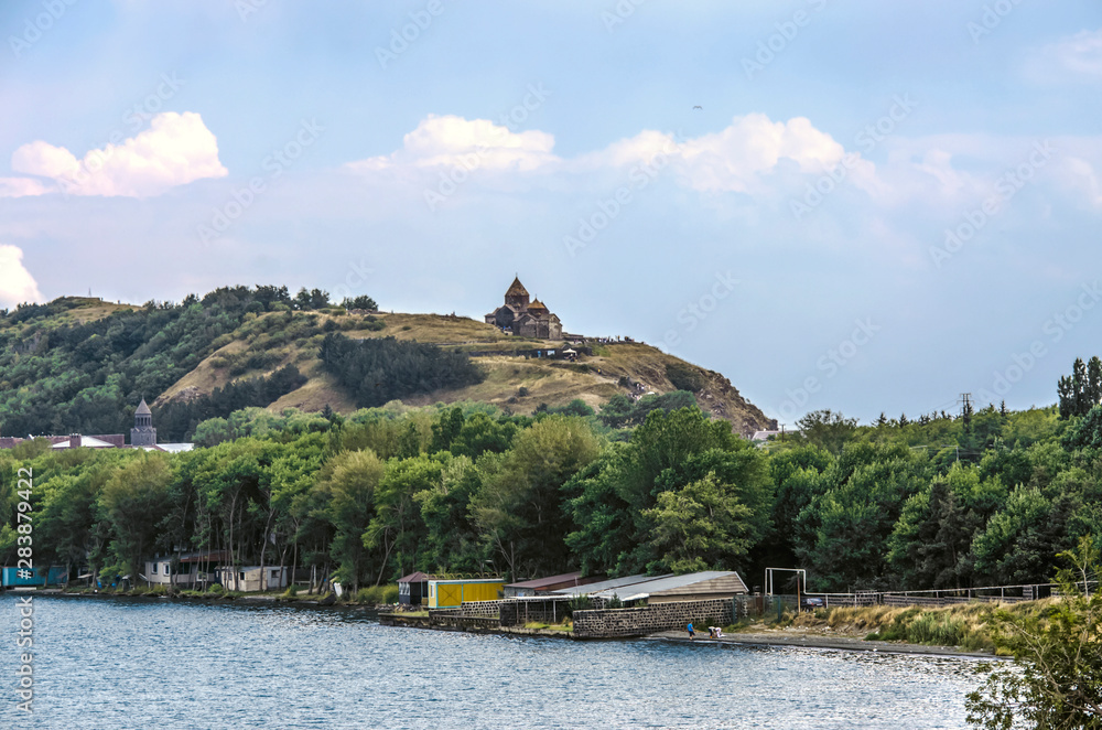 Shore on the peninsula of lake Sevan, with buildings among trees and the hill with the medieval monastery of Sevan in the Gegharkunik province of Armenia Shore on the peninsula of lake Sevan, with buildings among trees and the hill with the medieval monastery of Sevan in the Gegharkunik province of Armenia