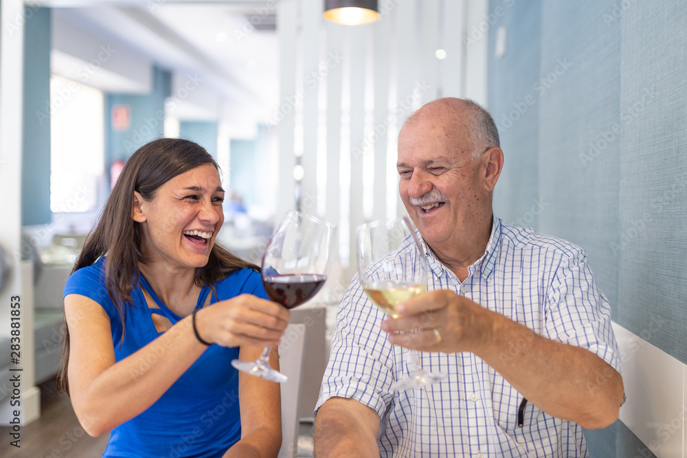 Mature man and young woman enjoying and smiling, spending time together..toasting with a glass of wine Mature man and young woman enjoying and smiling, spending time together..toasting with a glass of wine