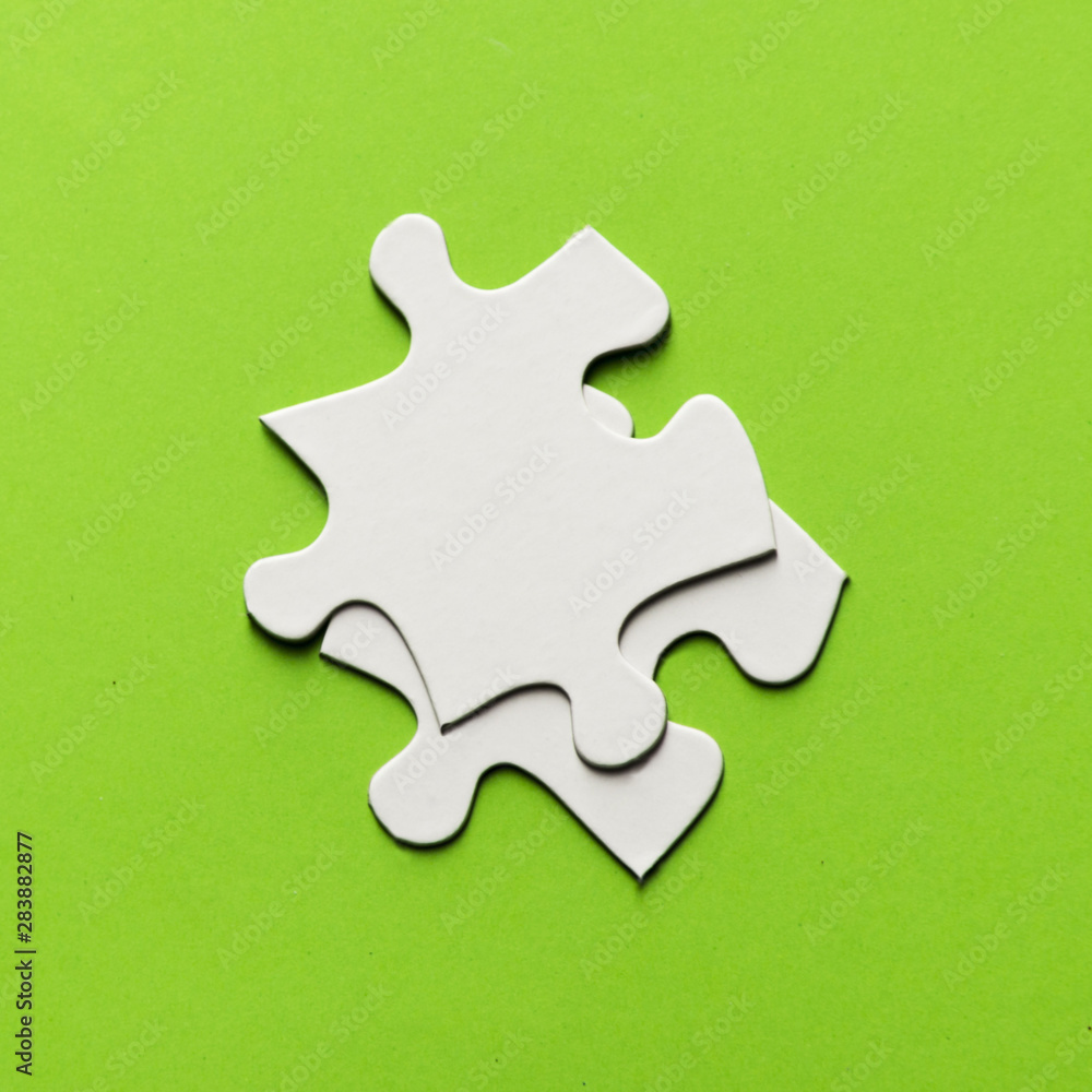 Fototapeta premium Two white jigsaw puzzle piece on bright green backdrop