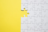 White jigsaw puzzle with one missing piece on yellow backdrop