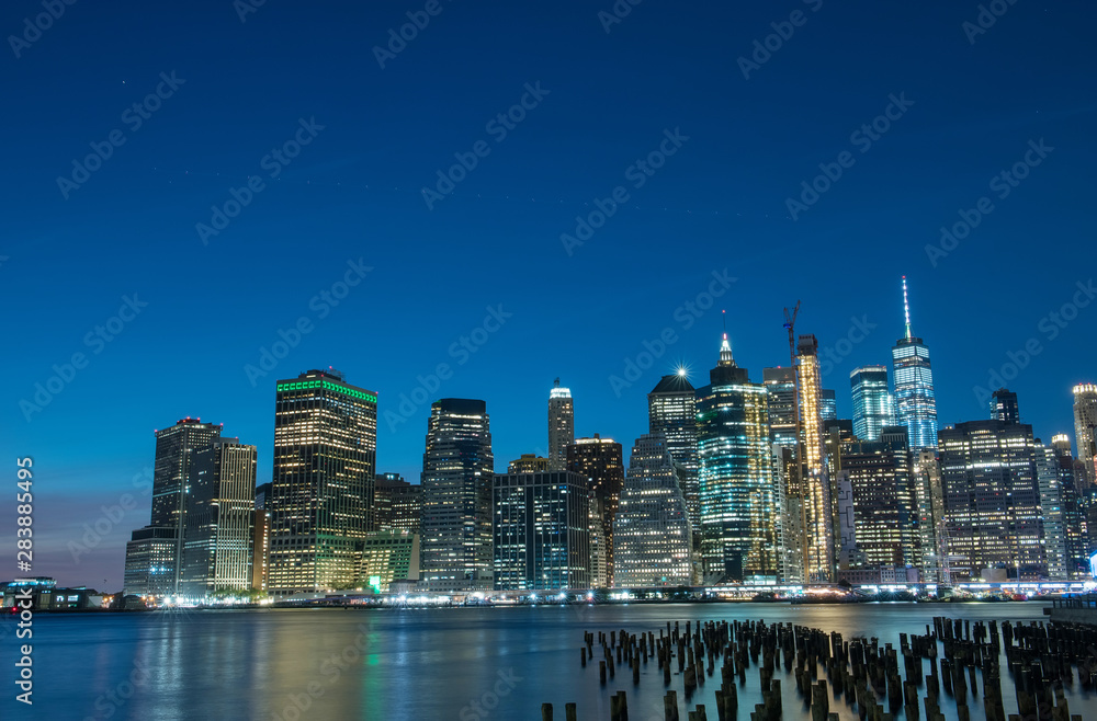 Fototapeta premium View from the water of the bay on the night city center of New York at sunset. Skyscrapers glowing in the dark against the sunset sky.