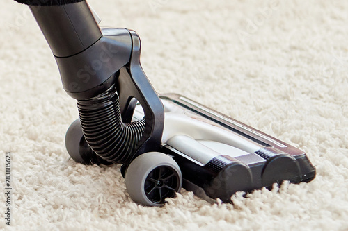 Close up of modern vacuum cleaner on beige carpet on floor in living room, copy space. Housework, household, spring-cleaning and chores concept. House cleaning