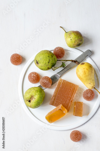 Homemade fruit marmalade and fresh pears on a round white dish on a light wooden background. Selective focus.