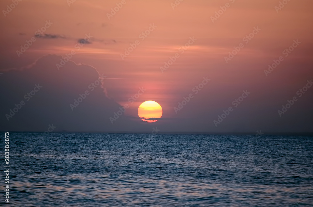 Sunset over calm sea water in pink evening clouds