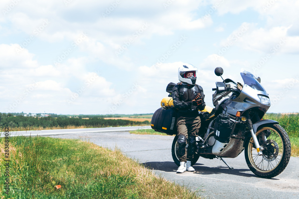 Fototapeta premium Dziewczyna kierowca w sprzęcie ochronnym, żółw. kamizelka kuloodporna. Motocykl przygodowy z bocznymi torbami. wycieczka motocyklowa. Na wolnym powietrzu. Świat podróż na dwóch kołach, koncepcja wolności. skopiuj spase