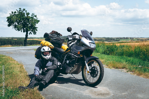 A male driver in a raincoat is sitting by adventure motorbike with side bags. a motorcycle tour journey. Outdoor road summer time. World travel on two wheels, freedom concept. rider equipment.