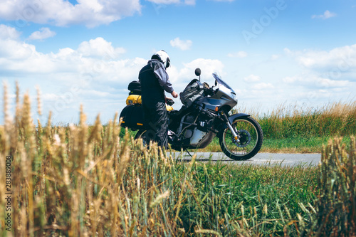Fototapeta Naklejka Na Ścianę i Meble -  A male driver in a raincoat is standing by adventure motorbike with side bags. a motorcycle tour journey. Outdoor. World travel on two wheels, freedom concept. rider equipment.
