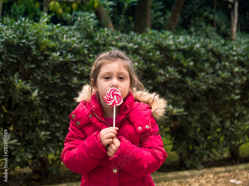 Happy young little child girl kid bite sweet lollipop candy. Portrait of a smiling girl with a lollipop in summer time