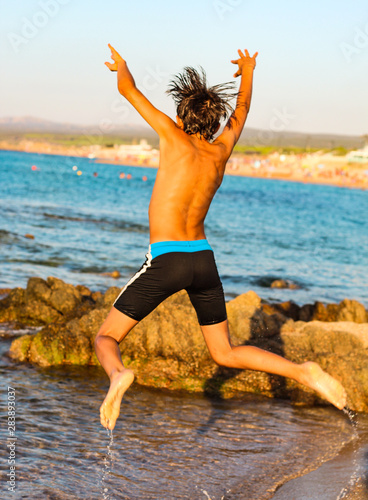 Heureux garçon saute et joue et avec l'eau sur la plage	