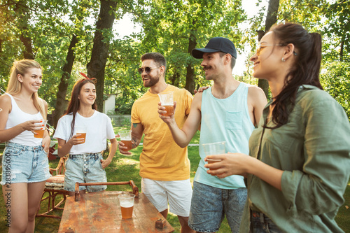 Group of happy friends having beer and barbecue party at sunny day. Resting together outdoor in a forest glade or backyard. Celebrating and relaxing  laughting. Summer lifestyle  friendship concept.