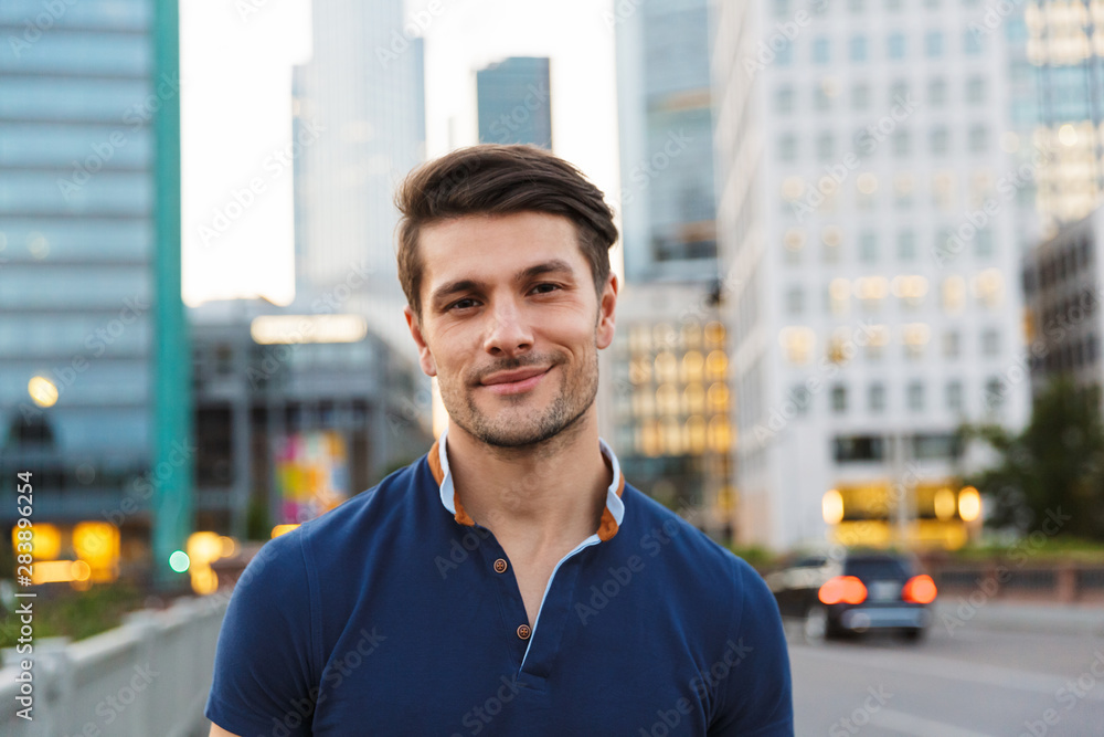 Cheerful young man walking outdoors by street in city looking camera. Cheerful young man walking outdoors by street in city looking camera.