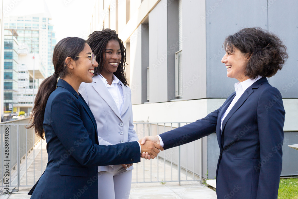 Two smiling businesswomen shaking hands outdoor. Cheerful African American and Caucasian woman meeting in summer park. Communication concept Two smiling businesswomen shaking hands outdoor. Cheerful African American and Caucasian woman meeting in summer park. Communication concept