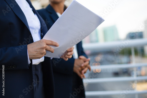 Partial view of businesswomen with papers. Mid section of female colleagues in formal wear holding documents outdoor. Paperwork concept © Mangostar