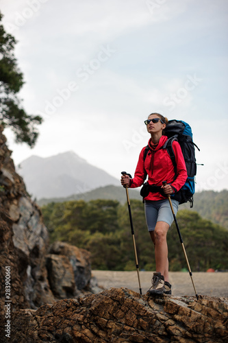 Slim fit woman in special wear standing with hiking backpack and sticks on the rock