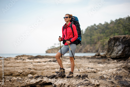 Girl in special wear standing with hiking backpack and sticks on the rock