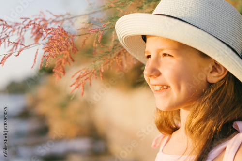 Pretty little girl with long beautiful hair in a straw hat and a pink dress in a summer beach. Sunny day, sunset.