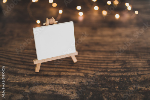 blank canvas miniature surrounded by fairy lights on wooden desk photo
