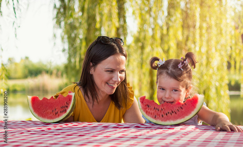 Mother and daughter eating watermelon slice on a picnic In a park