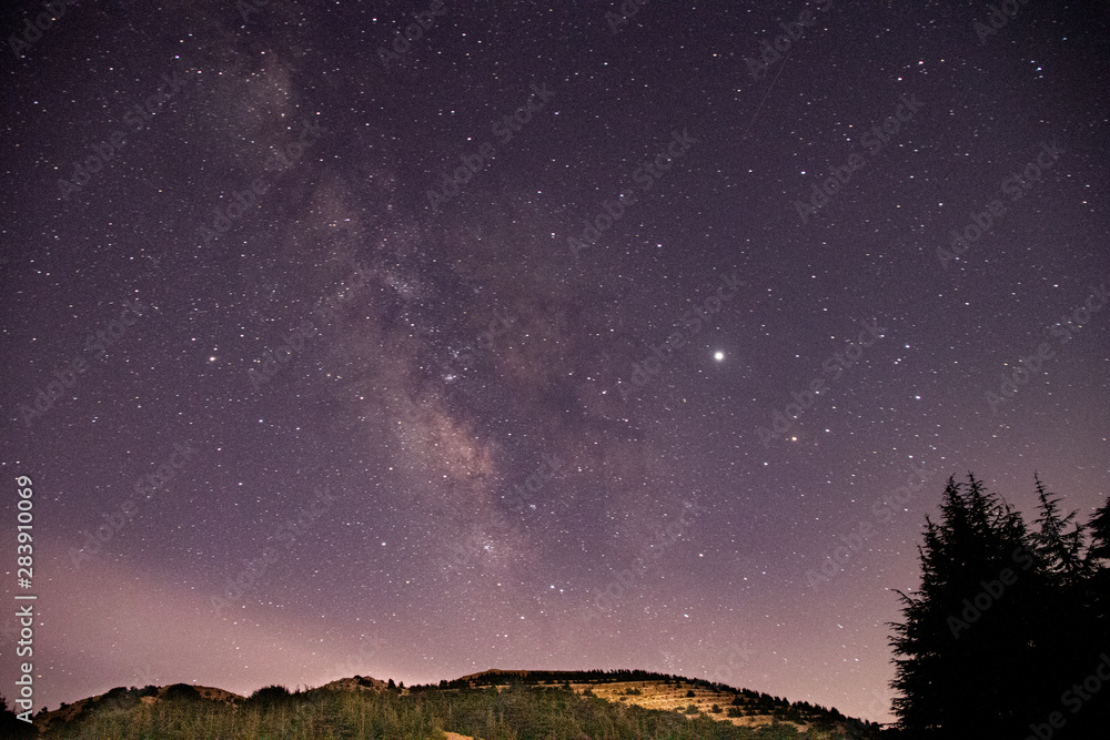 Beautiful clear night landscape and scenery. Starry sky with milky way galaxy over the mountains and the cedar trees.