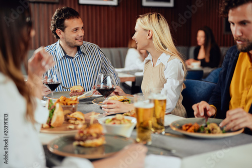 Multiethnic friends sitting at restaurant  drinking alcohol  chatting and having burgers for dinner.