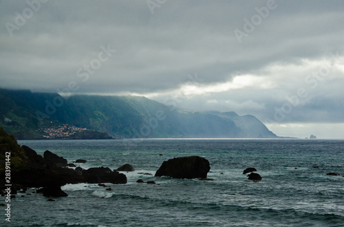 Dunkle Wolken liegen über der Bucht von Sao Vincente, Madeira, Portugal, Europa und verdunkeln die Szenerie. An einer Stelle beleuchten helle Sonnenstrahlen den Ozean.